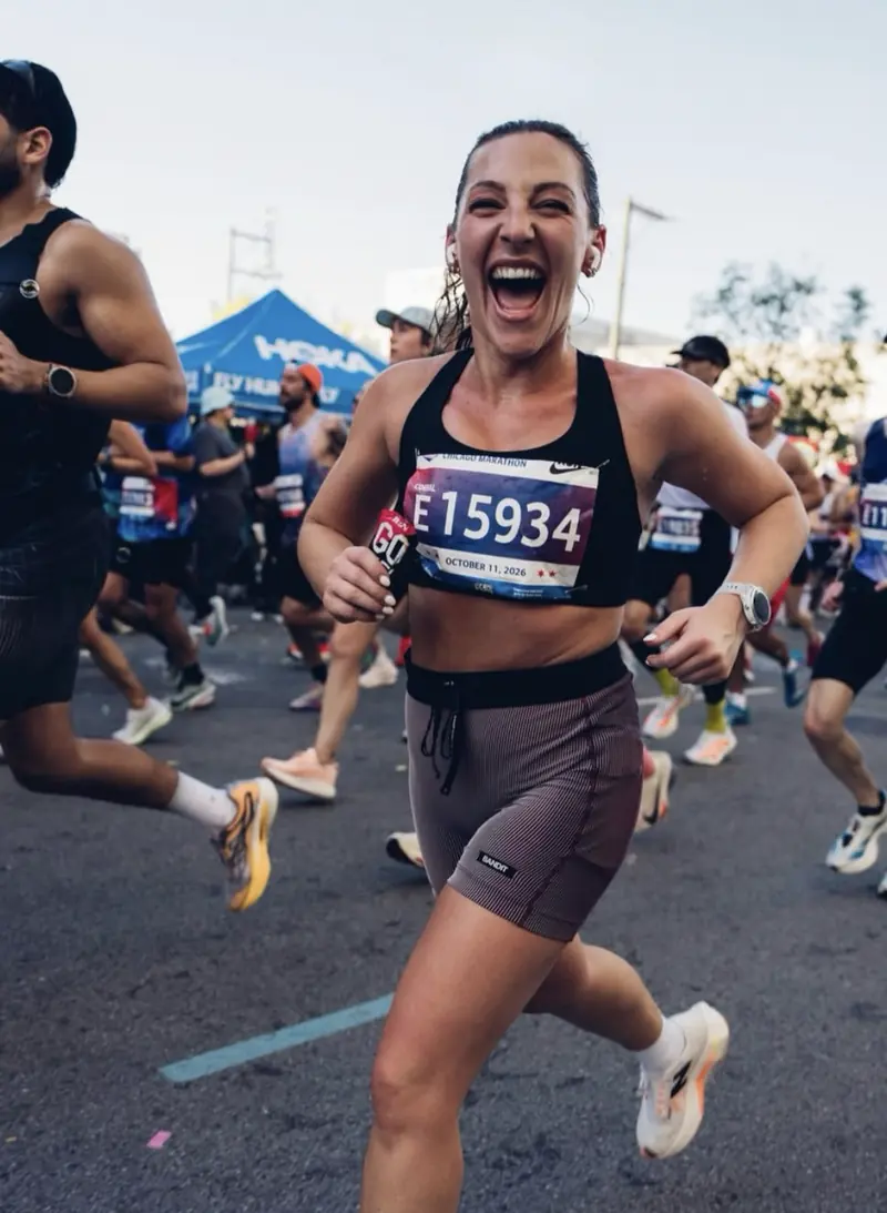Sam Hendel running a race, smiling, in a black top and mauve shorts